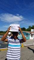 Man smiling while lifting a KC paper name in the air under a bright blue sky, showing joy and local pride