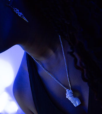 A beautiful black woman wearing a necklace with a resin woman's torso wrapped in a wire Shabari tie instead of bondage rope. It is on a stainless-steel curb chain. Her earring is made from a single byzantine chainmail link with a spike on the end.