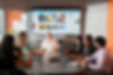 Employees around conference room table listening to man at head of table presenting.