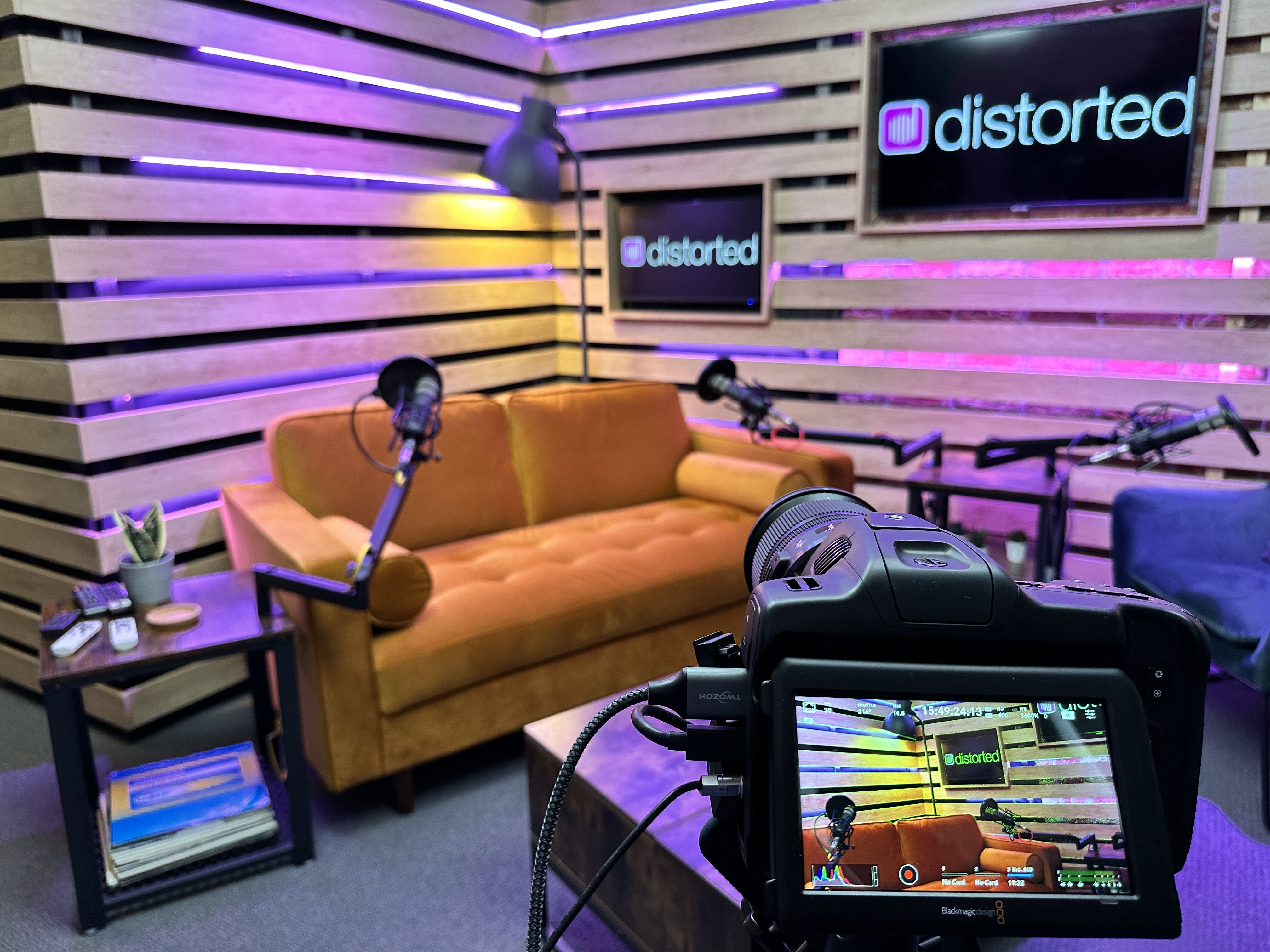 Distorted Leeds podcast studio with sofa, chairs, microphones, camera and illuminated backdrop