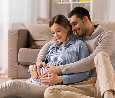 pregnancy, love and care concept - happy man hugging pregnant woman and making hand heart 