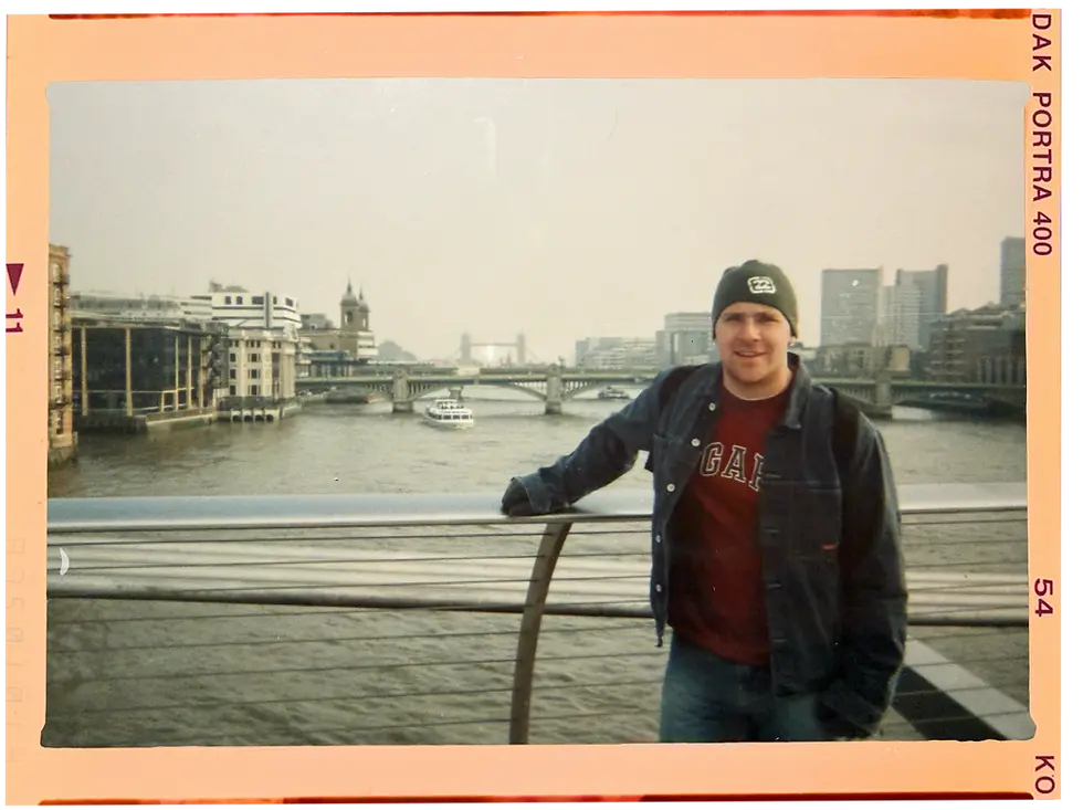 Man posing with a river and bridge in the background, London cityscape.