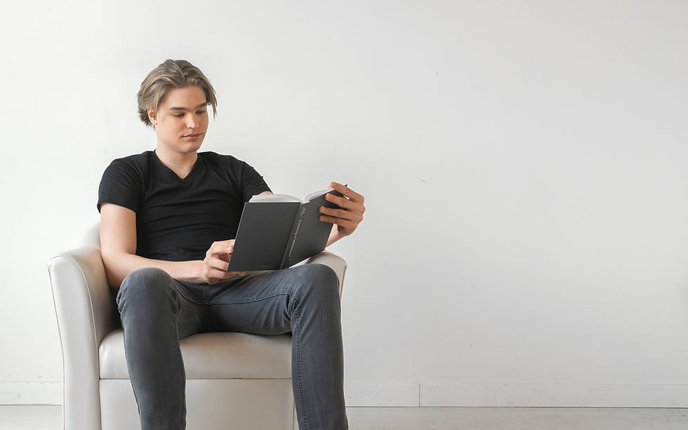 A student sits comfortably in an armchair against a minimalist white background, deeply engrossed in a book.