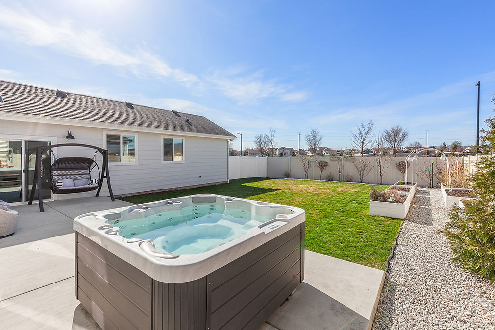 Backyard of home for sale in Northern Idaho, that shows ADU unit with hot tub, patio, and green lawn