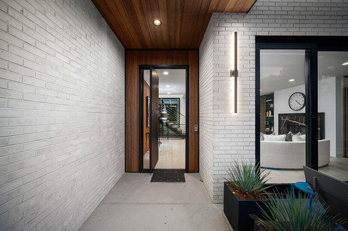 A clean-lined entryway framed by wood, glass, and steel offers a powerful introduction to the home’s modern style