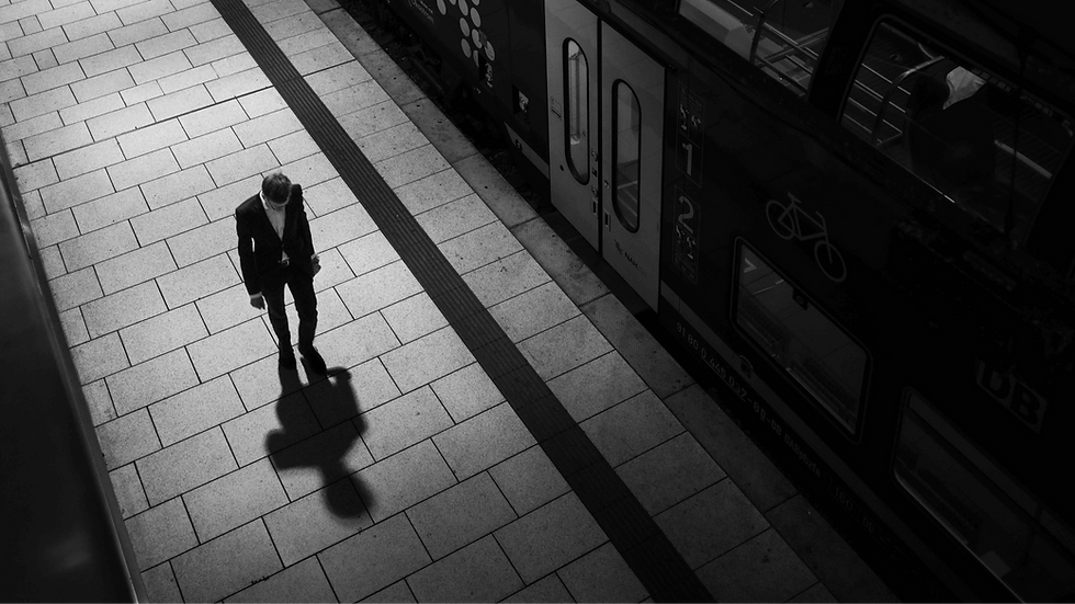 Minimal black-and-white fine art street photograph of a solitary figure walking beside a train platform, viewed from above, emphasizing light, shadow, geometry and urban observation.
