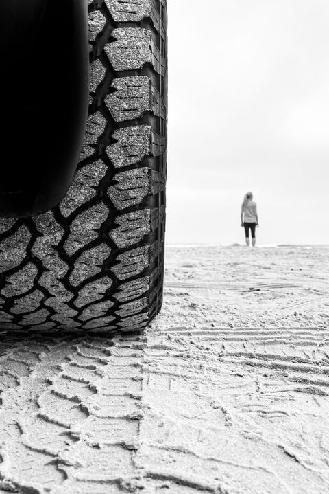 Black and white fine-art photograph – off-road tire in sand with a distant figure – svensonphoto