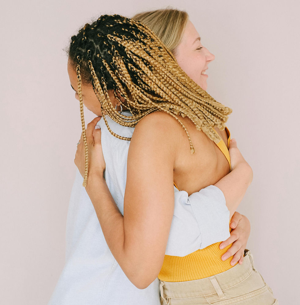 Two women embracing warmly, wearing light colors. The background is plain and light, creating a serene and joyful mood.