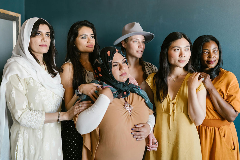 Diverse group of six women standing together against a blue wall, some holding hands, wearing colorful outfits, with a calm, supportive mood.