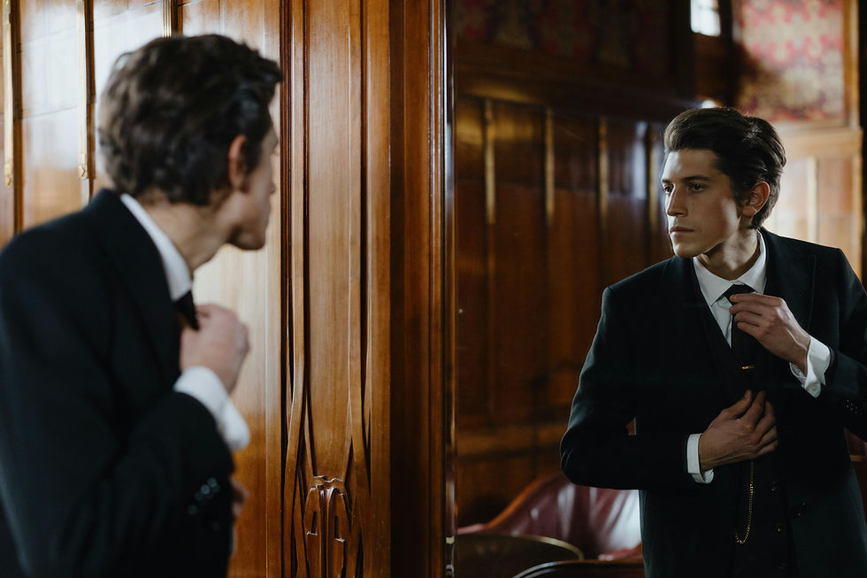 A man in a suit adjusts his tie while looking in a mirror, set in a wood-paneled room with vintage decor.