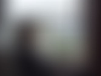 Sullen elderly woman in a wheelchair gazes out a window at city buildings. Soft lighting creates a contemplative mood.