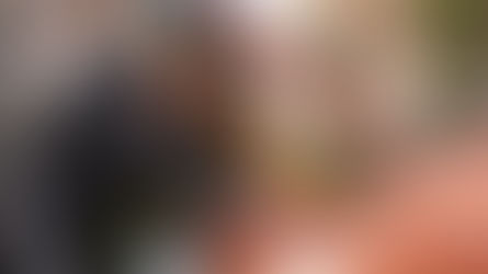 Homem verificando o motor de um carro com o capô aberto enquanto uma mulher observa ao fundo, em ambiente externo durante o dia.