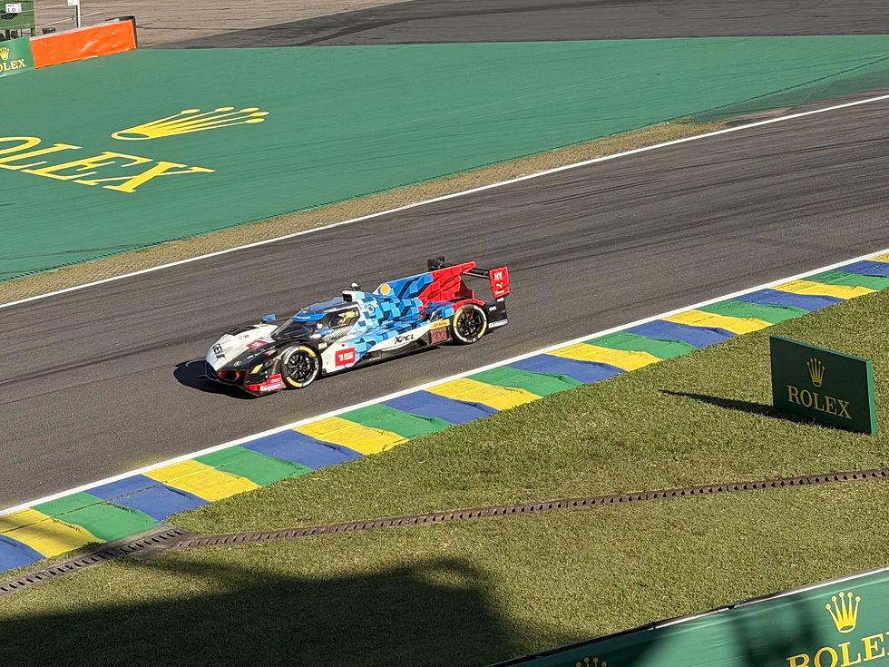 BMW M Hybrid V8 #15 percorre uma reta do Autódromo de Interlagos durante as 6 Horas de São Paulo. O hypercar exibe pintura especial em azul, vermelho, branco e preto, passando pelas zebras verde, amarela e azul da pista, com a área de escape e a marca Rolex ao fundo.