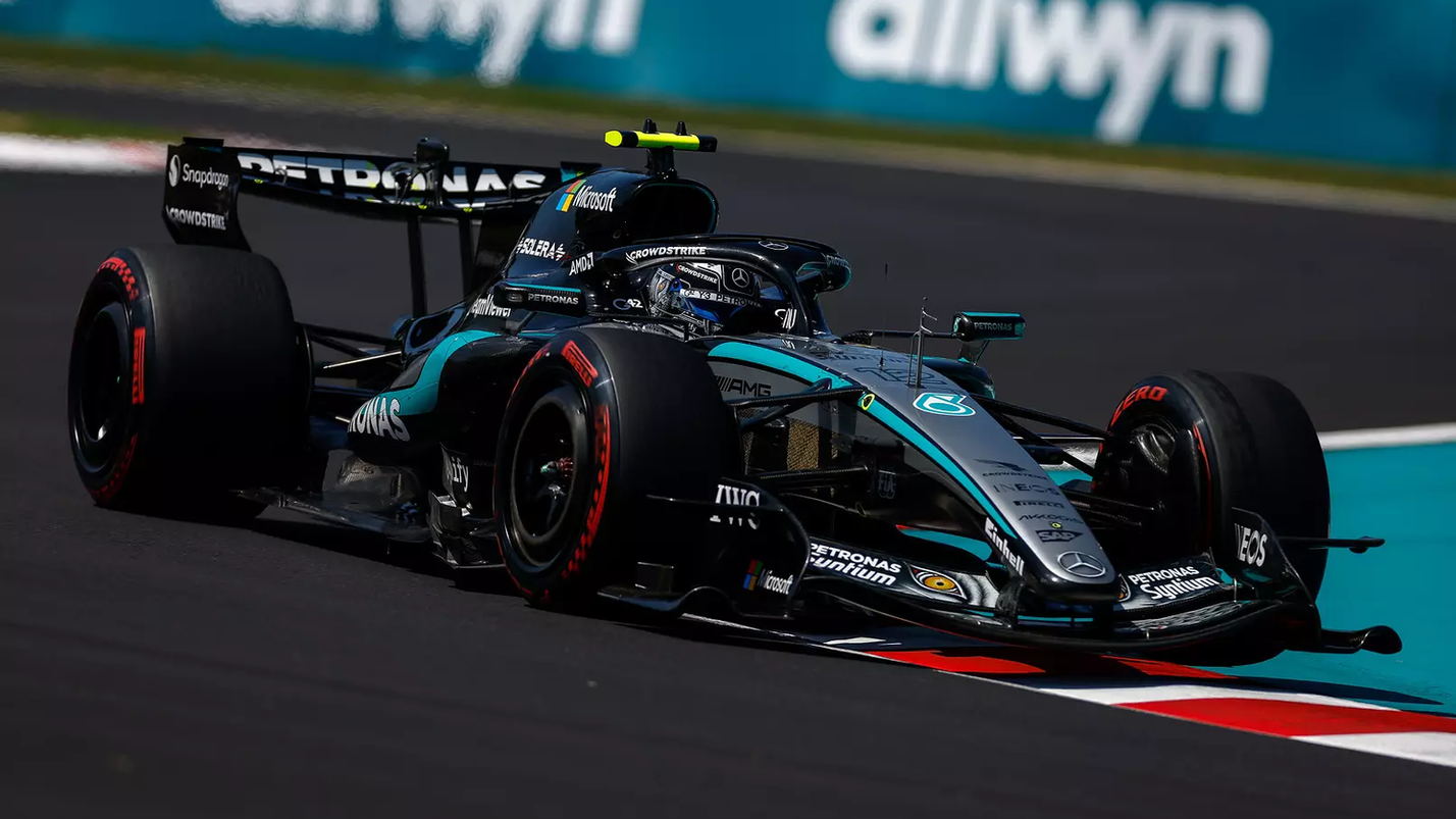 Carro de Fórmula 1 preto e prateado da Mercedes contornando curva em alta velocidade durante corrida, com pneus slick e pista seca