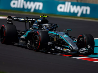 Carro de Fórmula 1 preto e prateado da Mercedes contornando curva em alta velocidade durante corrida, com pneus slick e pista seca
