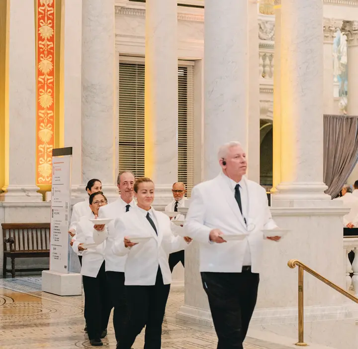 Servers walking with plates of food in a line