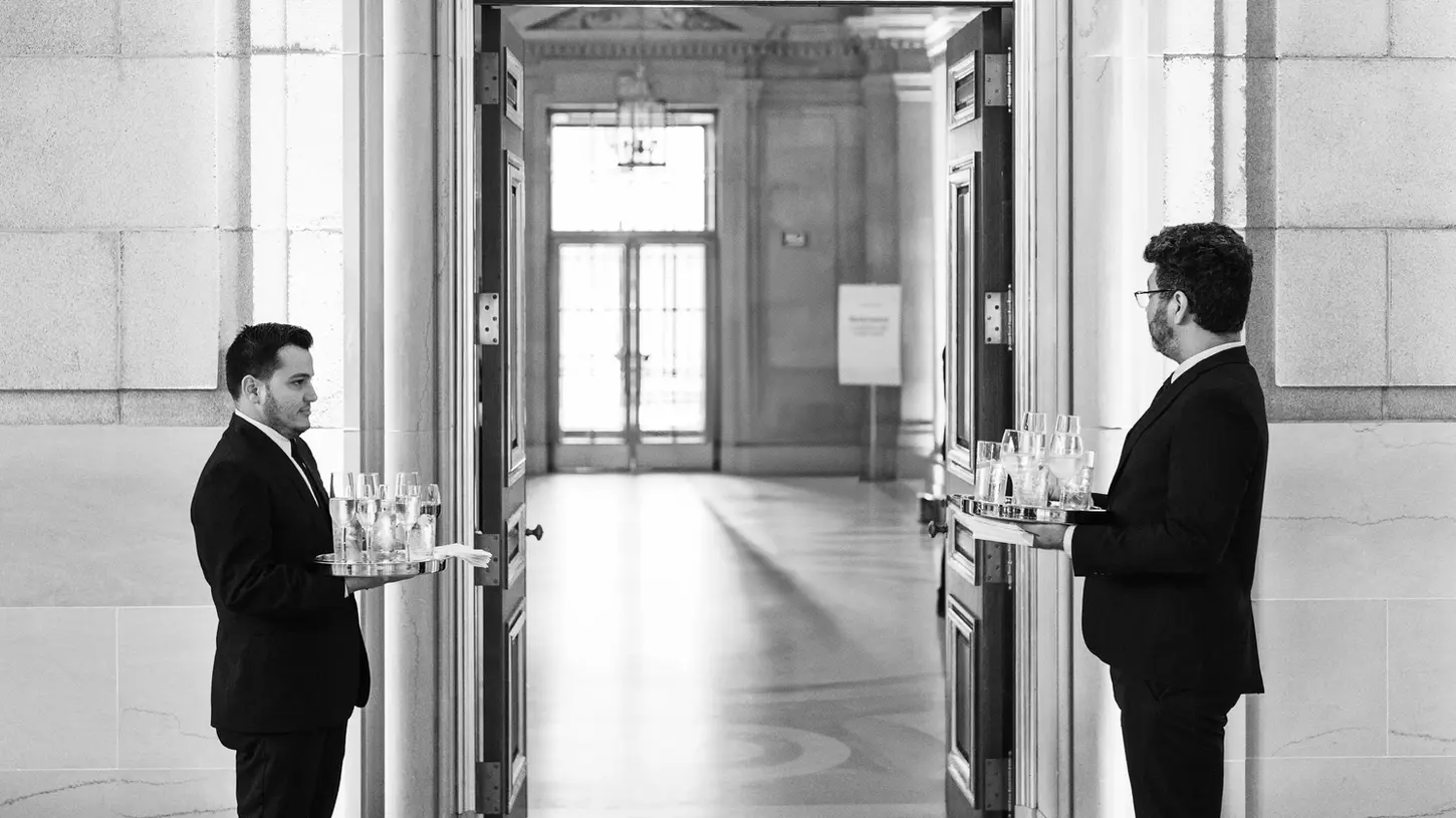 Two servers standing by event entrance offering wine and champagne