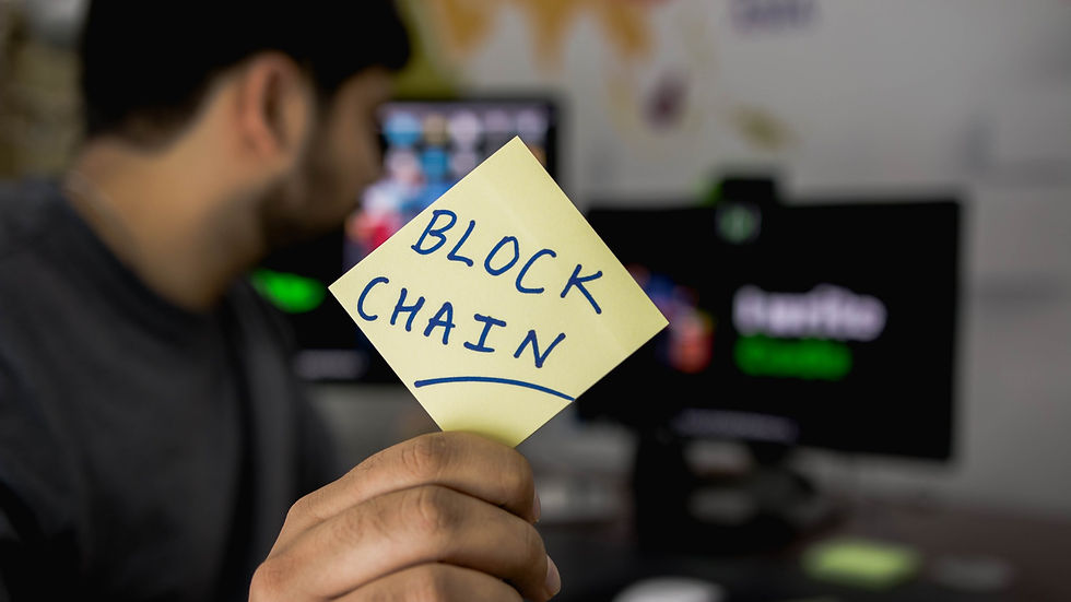 A photograph of a man sitting at his desk holding a post it with the words block chain