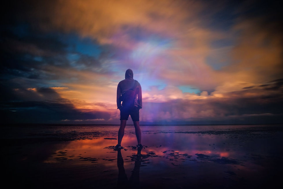 A photograph of a man standing by water and a wonderful sunset