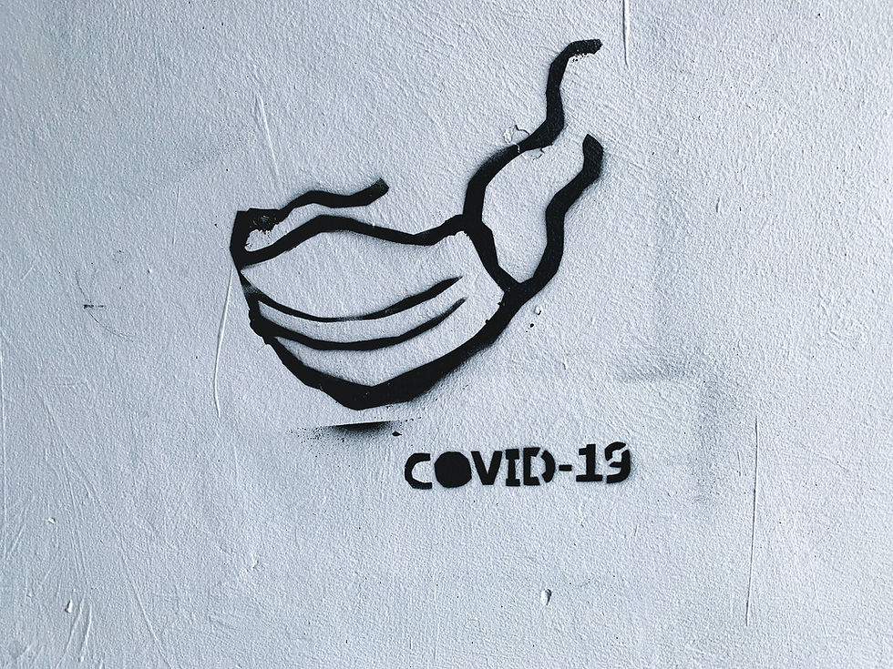 A Banksy-type graffiti of a mask and the words COVID-19 on a white wall