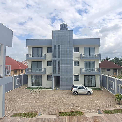 Modern three-story building with balconies, surrounded by a courtyard and a parked white c