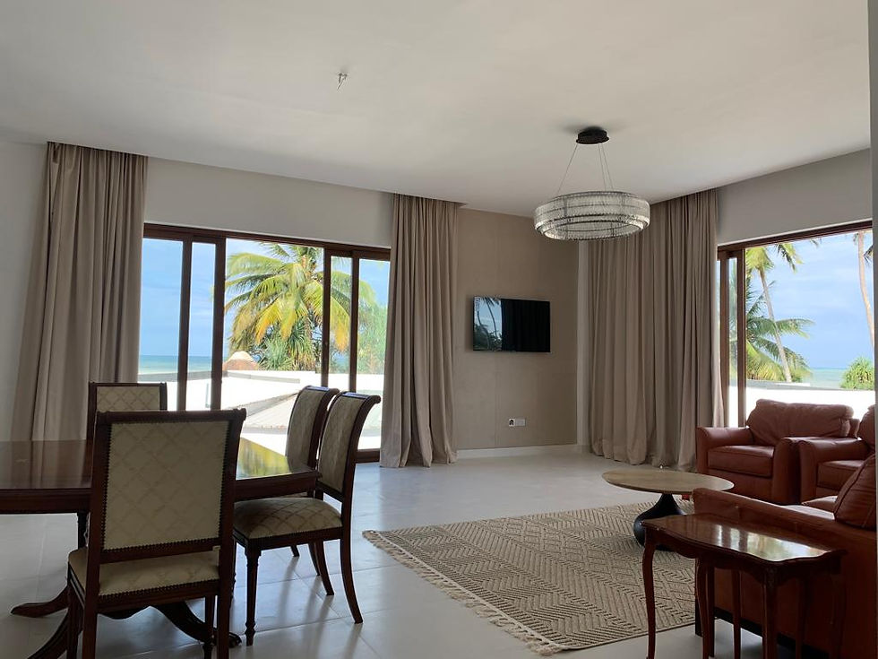 Spacious hotel living room with leather sofas, a wall-mounted TV, and panoramic views of the beach a