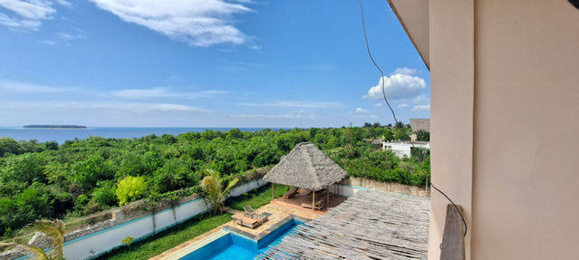 Sweeping ocean view from a villa balcony, with a thatched pool pavilion and vibrant green canopy stretching to the horizon