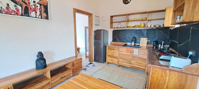 Fully fitted kitchen with slate tile backsplash, open wooden shelving, countertop appliances, and curtain-covered window