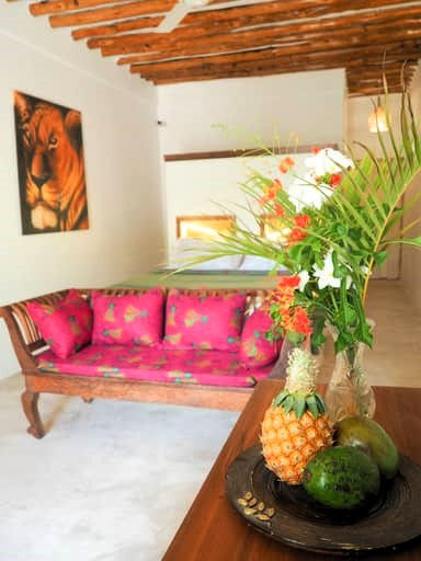 A bright room with a wooden bench featuring vivid pink cushions, a fruit arrangement on a 