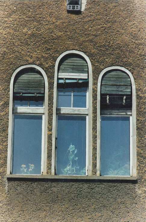 Trois fenêtres verticales cintrées sur une façade texturée à Berlin.