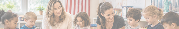 Teacher and five children smiling around a table in a bright classroom with red-and-white striped wall.