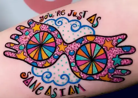 Tatuaje de gafas lunares coloridas con el texto: You're just as sane as I am.