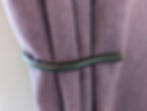 A purple curtain being held back by a handmade curtain holdback.