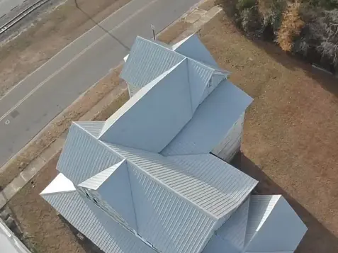 Overhead view of a tan home mid-metal roof replacement, showing detailed work by certified home roofing repair specialists.