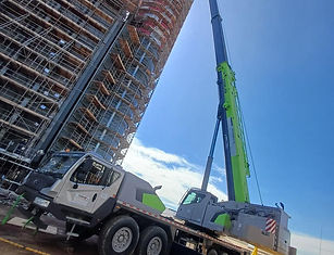 Guindaste zoomlion ZTC 1200V verde e cinza da Zoomlion em operação ao lado de edifício em fase de construção.