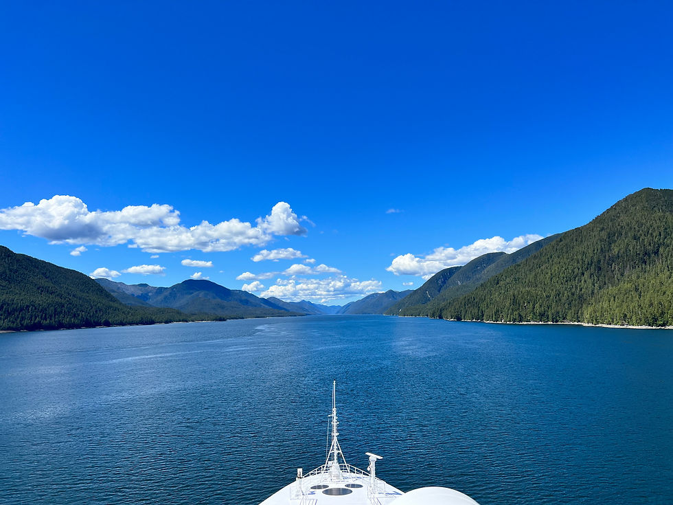 Cruise ship bow in blue ocean, surrounded by lush green mountains under a clear sky with scattered white clouds.