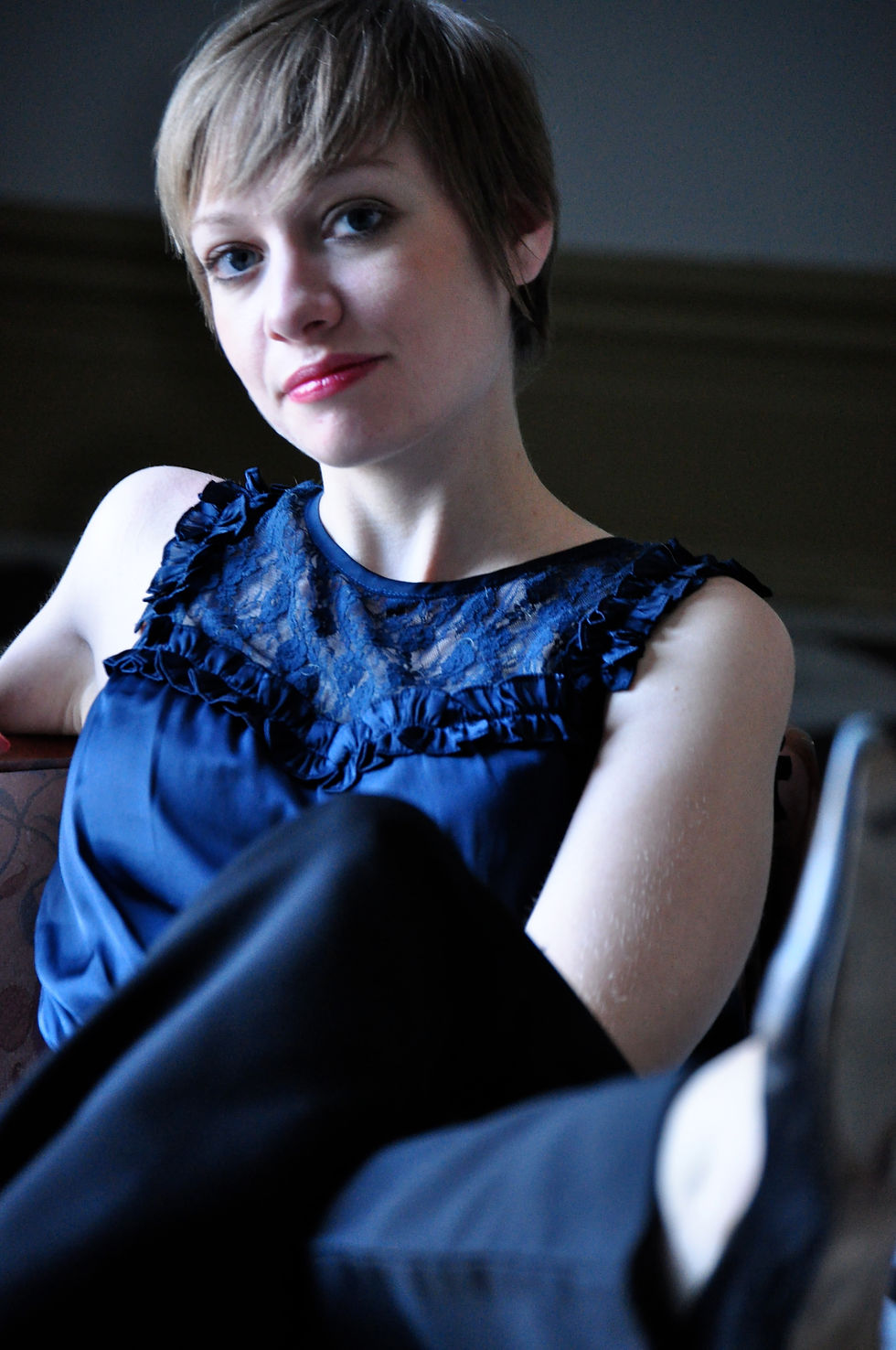 A woman in a blue shirt sits casually on a chair.