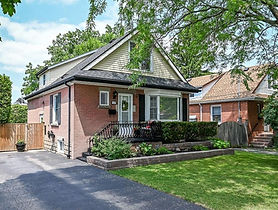 Front exterior of 180 East 25th Street in Hamilton, a brick one-and-a-half-storey detached home with a landscaped yard and private driveway.