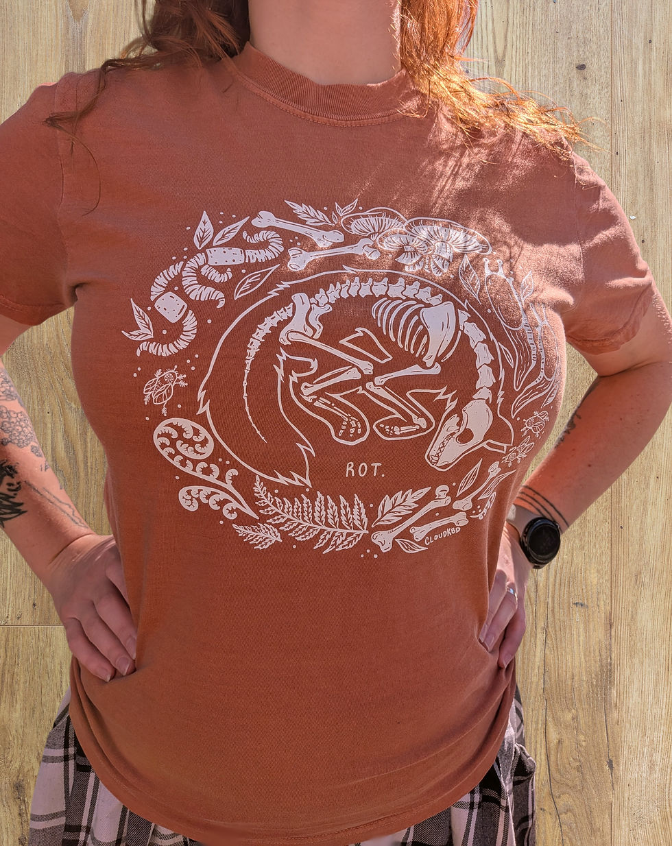 A femme person wears a shirt featuring a fox skeleton surrounded by nature. It reads, "Rot."
