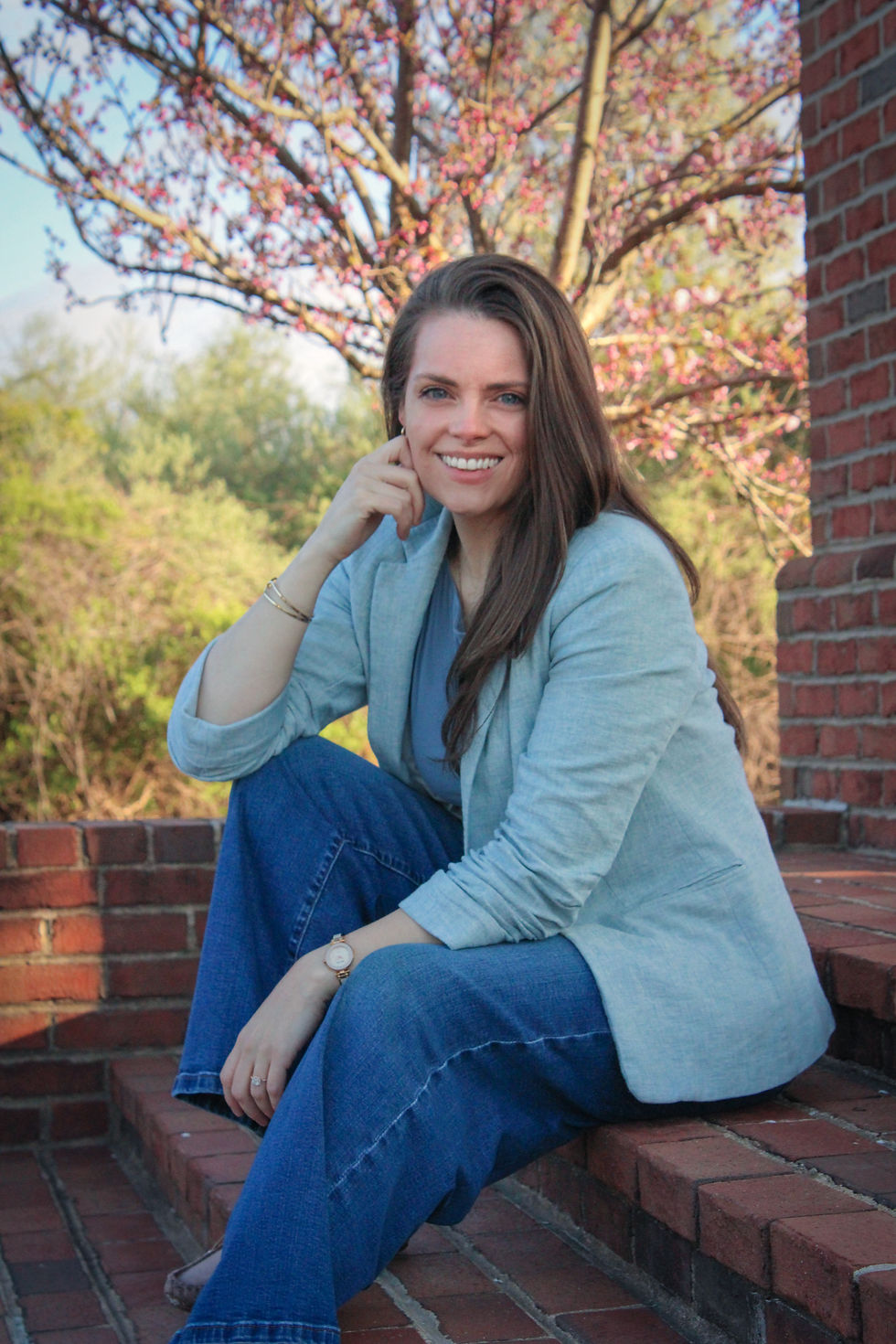 Portrait photo of woman with long hair smiling and sitting on brick steps.