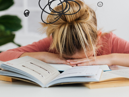 Exhausted woman experiencing burnout with head on desk and books scattered—symbol of mental overload and habit struggle.