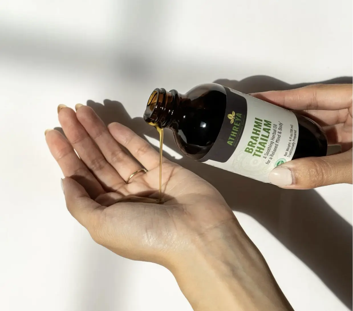 A woman pouring Brahmi Thailam (oil) by Athreya Herbs from a brown jar into her palm so she can oil her feet before bed.