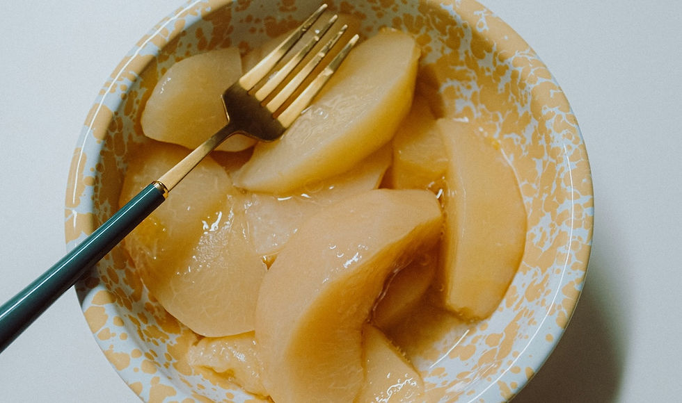 A close-up shot of warm, sliced pears prepared using gentle Pitta-pacifying food preparation methods, served with a dark spoon in a rustic ceramic bowl.