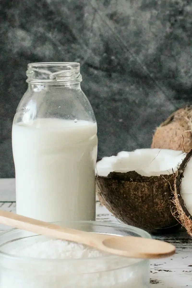 best massage oils: coconut oil in a jar, a broken coconut, and coconut flakes in a bowl with a wooden spoon