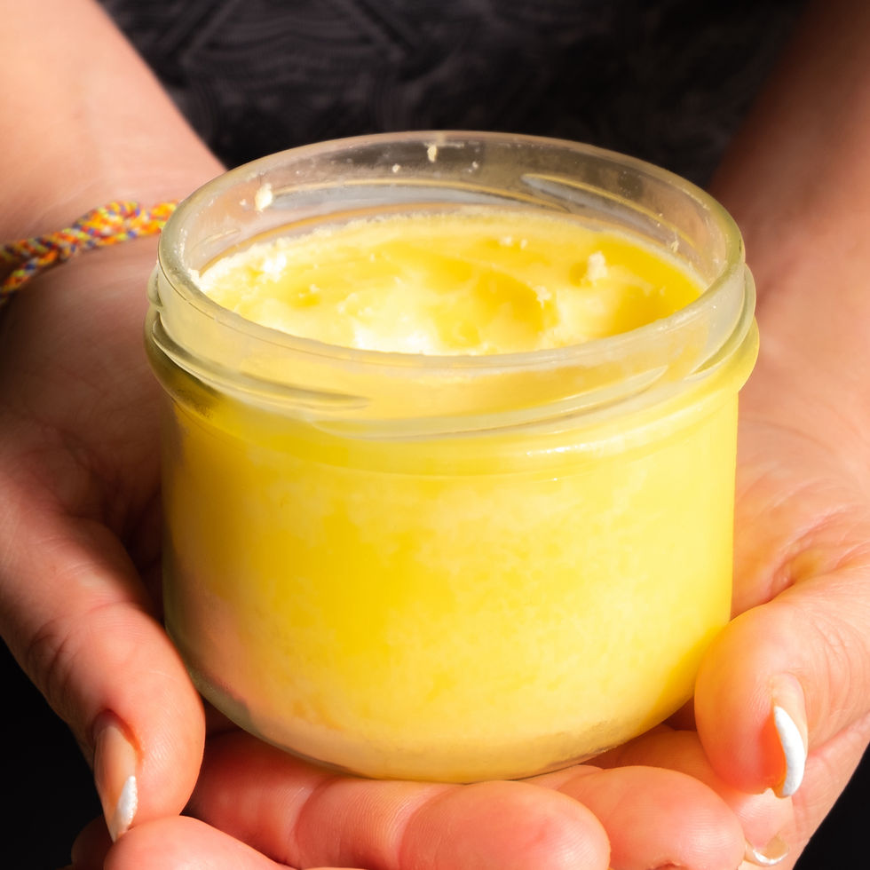 A close-up view of a jar of golden, clarified gheee being offered by a woman representing nourishing healthy fats for Ayurveda.