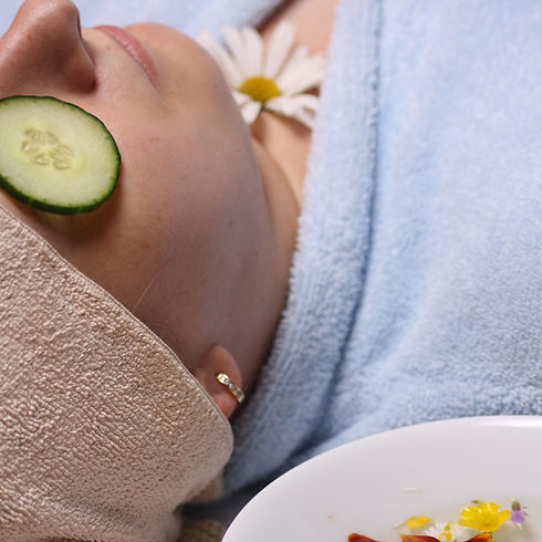 A woman over 40 resting comfortably on her back with fresh cucumber slices placed over her closed eyes, smiling gently.