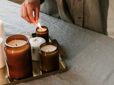 A woman finding rhythm over 40 lighting brown jar candles on a gold tray atop a gray tablecloth, creating a warm, cozy ambiance.