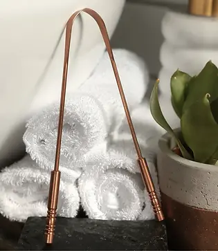 Ayurvedic copper tongue scraper against a background of white fluffy towels for oral hygiene as a morning detox ritual.