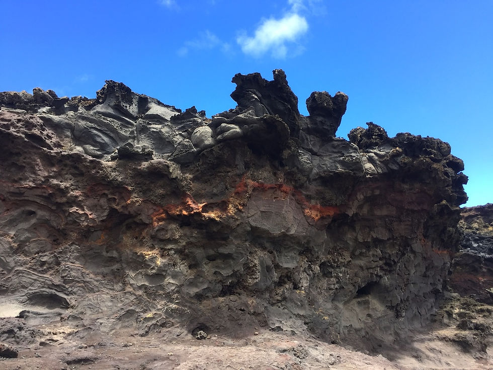 Volcanic dark lava rocks stacked along a Hawaiian coastline under a clear blue sky on Maui.
