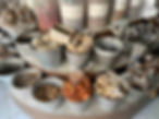 A vibrant outdoor herb and spice market stall in Chiang Rai, Thailand, displaying large silver buckets filled with traditional dried Ayurvedic herbs, cinnamon sticks, Sichuan pepper, and ground cooking spices.